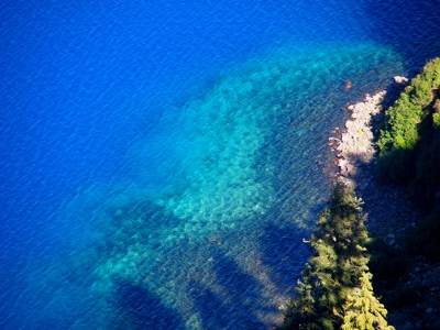 [The edges of the water near the rocks is a greenish blue and then becomes a black blue at the closest edges. The deeper water is a very pure blue.]